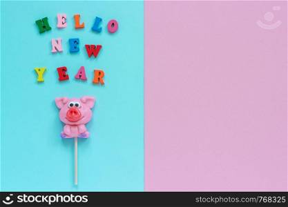 Funny pink pig lollipop and multicolor inscription Hello New Year on blue pink background. Top view Copy space Layout Concept greeting card Year of the pig.. pig lollipop and text Hello New Year
