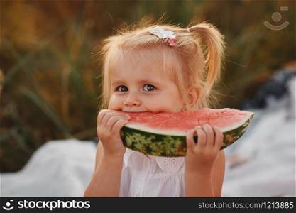 Funny portrait of an incredibly beautiful Red-haired little girl eating watermelon, healthy fruit snack, adorable toddler child with curly hair playing in a sunny garden on a hot summer day. portrait