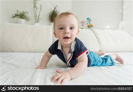 Funny portrait of baby boy crawling on bed and looking at camera
