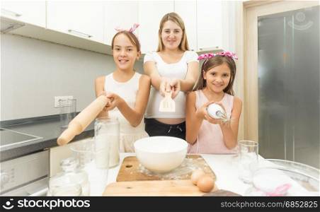 Funny portrait of family pointing utensils at camera on kitchen