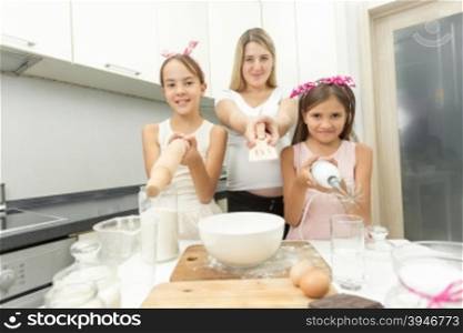 Funny portrait of mother and daughter pointing utensils at camera on kitchen