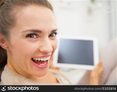 Funny portrait of smiling young woman sitting on divan and using tablet pc