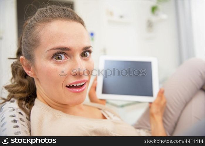 Funny portrait of surprised young woman sitting on divan and using tablet pc
