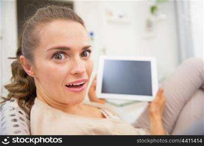 Funny portrait of surprised young woman sitting on divan and using tablet pc