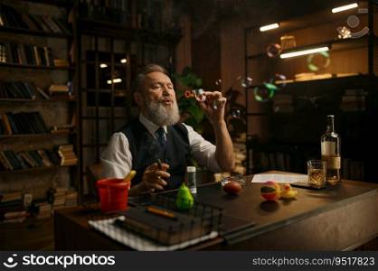 Funny relaxed senior businessman blowing up soap bubbles while sitting at work table. Funny relaxed senior businessman blowing up soap bubbles