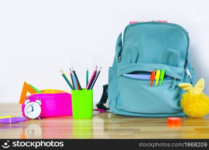 funny school backpack with markers, bright pencil case, fluffy keychain glass with colored pencils and an alarm clock on a wooden table. back to school concept.