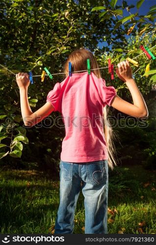 Funny shot of young girl hanging on clothesline at garden