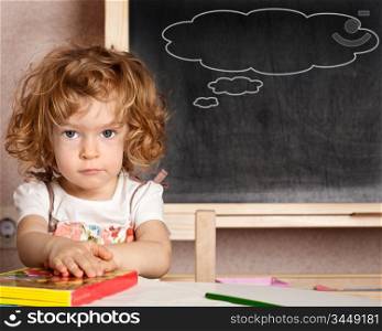 Funny smiling child in a class against blackboard with speech bubbles. School concept
