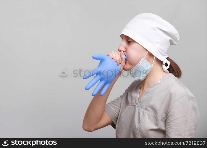 funny smiling female nurse or doctor in medical uniform and protective mask is inflating blue latex glove isolated on white background.. funny smiling female nurse or doctor in medical uniform and protective mask is inflating blue latex glove isolated on white background