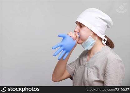 funny smiling female nurse or doctor in medical uniform and protective mask is inflating blue latex glove isolated on white background.. funny smiling female nurse or doctor in medical uniform and protective mask is inflating blue latex glove isolated on white background