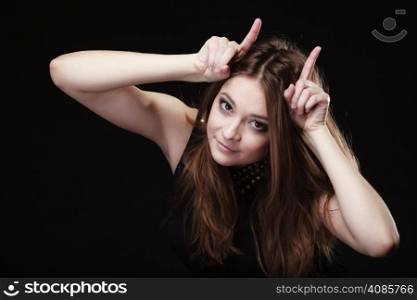 Funny teen naughty girl making devil horns with her fingers on black