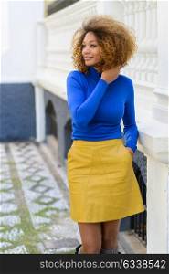 Funny young African American woman, model of fashion, smiling with afro hairstyle and green eyes wearing blue sweater and yellow skirt in urban background