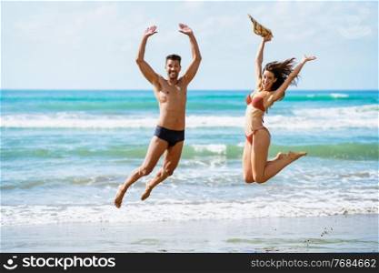 Funny young couple with beautiful bodies in swimwear jumping on a tropical beach.. Funny young couple with beautiful bodies jumping on a tropical beach.