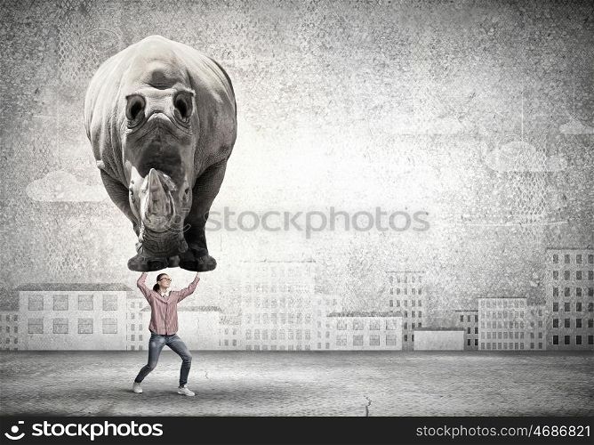 Funny young girl making effort to lift huge rhino. I am strong enough to do it