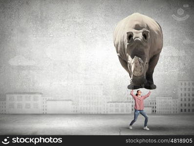 Funny young girl making effort to lift huge rhino. I am strong enough to do it