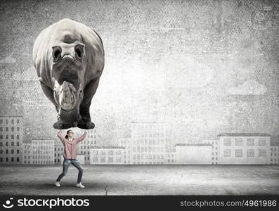 Funny young girl making effort to lift huge rhino. I am strong enough to do it