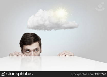 Funny young man looking from under table. Hiding under table