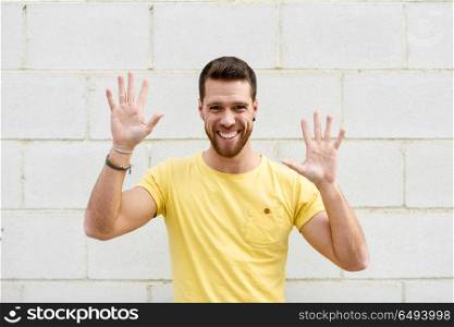 Funny young man on brick wall with open hands smiling.. Funny young man on brick wall with open hands smiling. Guy wearing casual clothes in urban background.