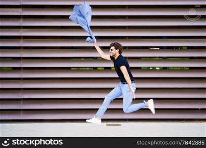 Funny young man wearing a suit jumping outdoors. Happy businessman in urban background.. Young man wearing a suit jumping outdoors