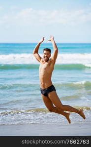 Funny young man with beautiful body in swimwear jumping on a tropical beach.. Young man with beautiful body in swimwear jumping on a tropical beach.