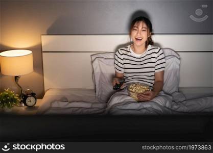 funny young woman watching TV and laughing on a bed at night