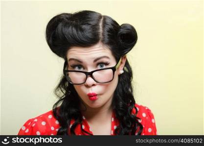 Funny young woman with pin-up make-up and hairstyle posing over yellow background