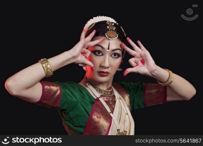 Furious young woman performing Bharatanatyam on black background