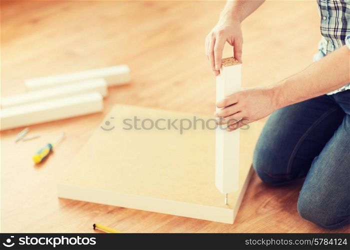 furniture, home and moving concept - close up of male hands assemblying legs to table