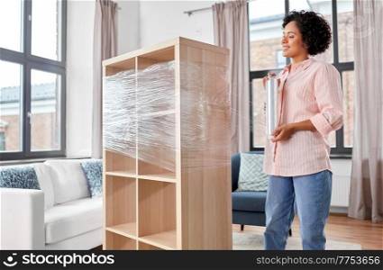 furniture, people and real estate concept - smiling happy woman packing shelf with plastic wrap and moving to new home. happy woman packing shelf and moving to new home