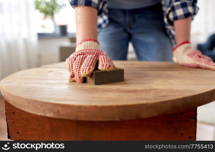 furniture renovation, diy and home improvement concept - close up of woman sanding old wooden table with sponge. woman sanding old round wooden table with sponge