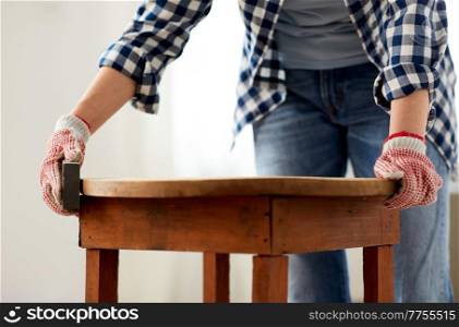 furniture renovation, diy and home improvement concept - close up of woman sanding old wooden table with sponge. woman sanding old round wooden table with sponge