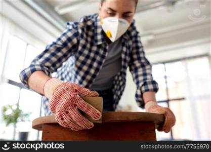 furniture renovation, diy and home improvement concept - close up of woman in respirator sanding old wooden table with sponge. woman in respirator sanding old table with sponge
