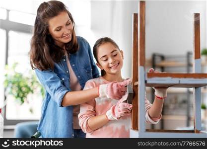 furniture renovation, diy and home improvement concept - happy smiling mother and daughter sanding old round wooden table with sponge at home. mother and daughter sanding old table with sponge