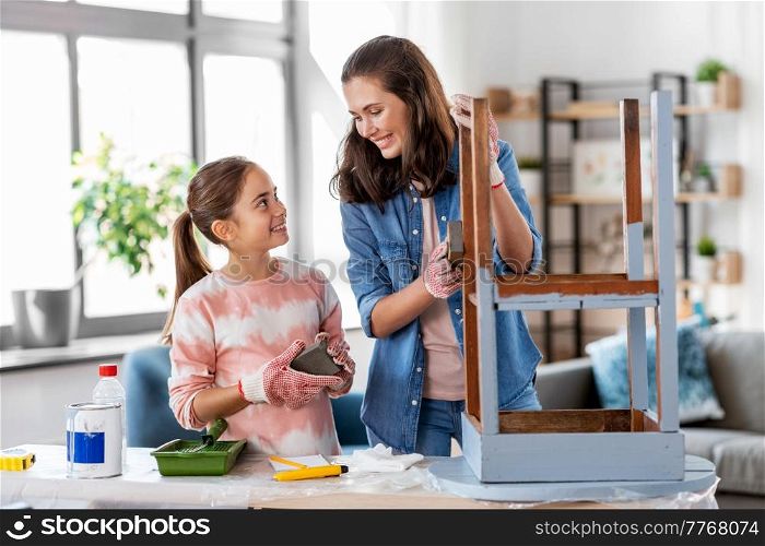 furniture renovation, diy and home improvement concept - happy smiling mother and daughter sanding old round wooden table with sponge at home. mother and daughter sanding old table with sponge