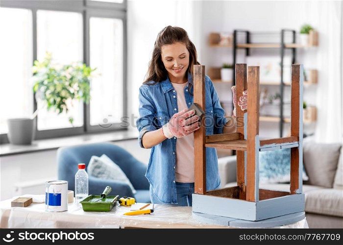 furniture renovation, diy and home improvement concept - happy smiling woman sanding old wooden table with sponge. woman sanding old round wooden table with sponge