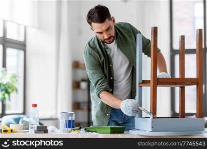 furniture renovation, diy and home improvement concept - man in gloves with paint brush painting old wooden table in grey color. man painting old wooden table in grey color