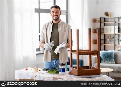 furniture restoration, diy and home improvement concept - happy smiling man applying solvent to rag and renovating old wooden table. man applying solvent to rag for cleaning old table