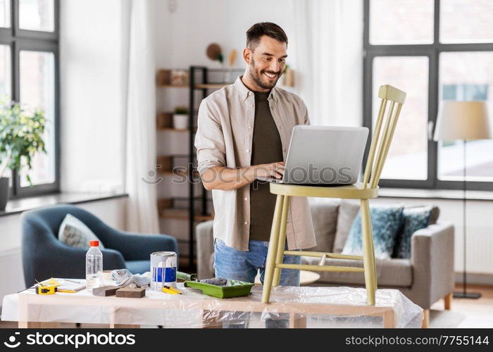 furniture restoration, diy and home improvement concept - happy smiling man with laptop preparing old wooden chair for renovation. man with laptop preparing old chair for renovation