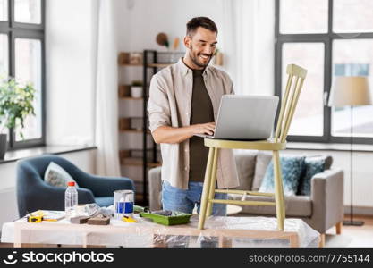 furniture restoration, diy and home improvement concept - happy smiling man with laptop preparing old wooden chair for renovation. man with laptop preparing old chair for renovation