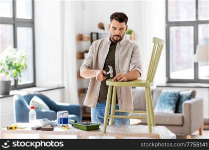 furniture restoration, diy and home improvement concept - man with hammer and nail repairing old wooden chair. man with hammer repairing old wooden chair at home
