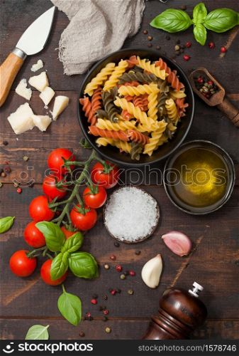 Fusilli pasta in black bowl with parmesan cheese and tomatoes, oil and garlic with basil and linen towel on wooden background. Top view