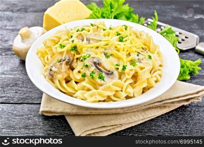 Fusilli pasta with mushrooms in creamy sauce, parsley and grated cheese in a plate on napkin on wooden board background