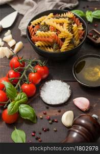 Fusilli tricolor pasta with parmesan and tomatoes, parmesan cheese and tomatoes on wooden table background with salt and pepper