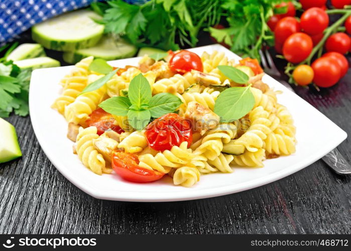 Fusilli with chicken, zucchini and tomatoes in a plate, napkin, fork, basil and parsley on wooden board background