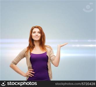 future, advertising and people concept - smiling teenage girl in casual clothes holding something on her palm over gray background with laser light