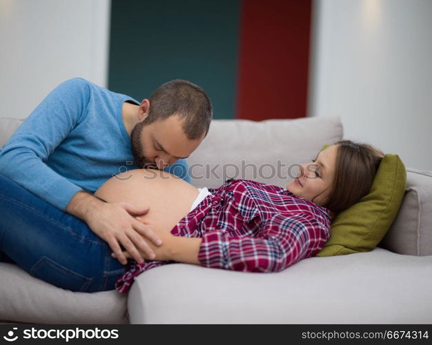 future dad listening the belly of his pregnant wife. Happy future dad listening the belly of his pregnant wife while relaxing on sofa at home