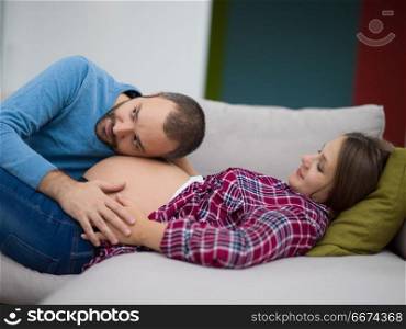 future dad listening the belly of his pregnant wife. Happy future dad listening the belly of his pregnant wife while relaxing on sofa at home
