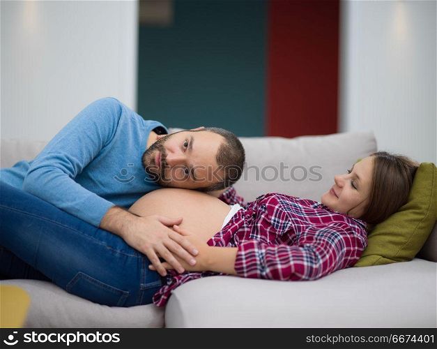 future dad listening the belly of his pregnant wife. Happy future dad listening the belly of his pregnant wife while relaxing on sofa at home