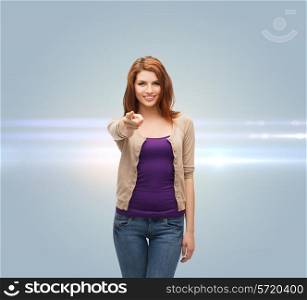 future, gesture and people concept - smiling teenage girl in casual clothes pointing finger on you over gray background with laser light