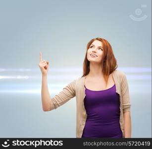 future, gesture and people concept - smiling teenage girl in casual clothes pointing finger up over gray background with laser light